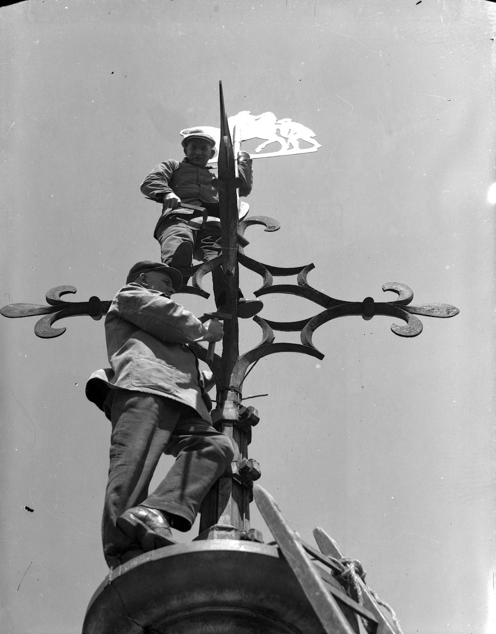 Twee werklieden die de windwijzer op de spits van de Domtoren Domplein schoonmaken 1940