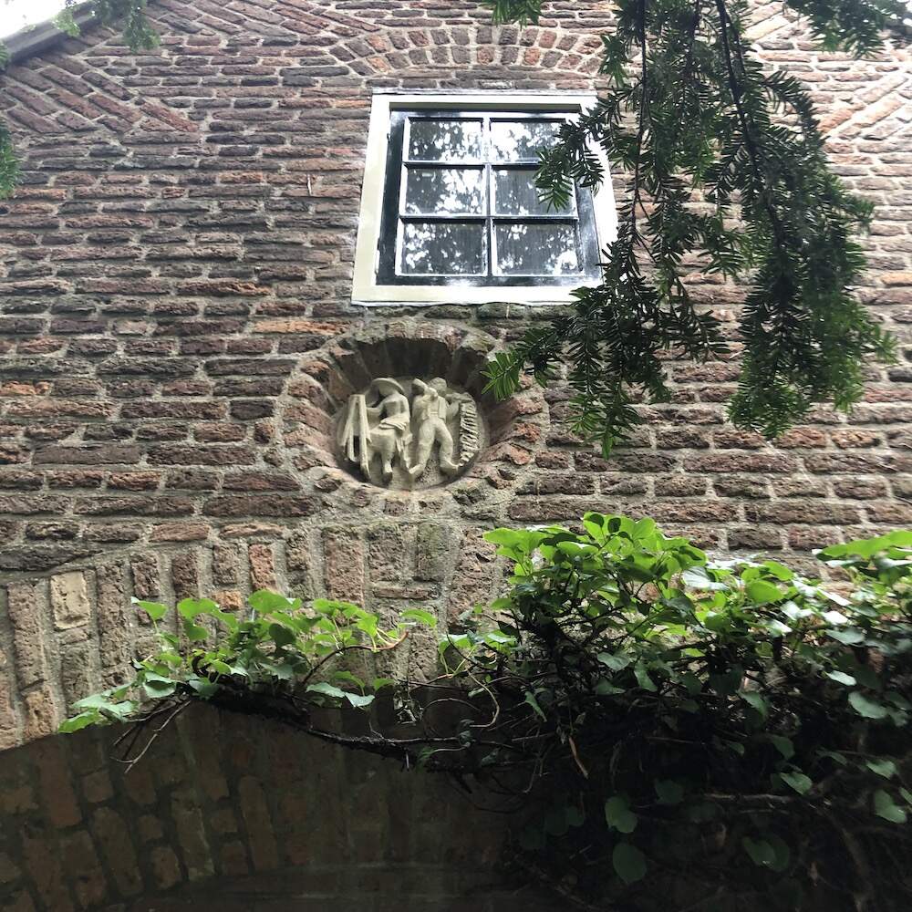 Gevelsteen op woonhuis met beeldhouwer aan het werk